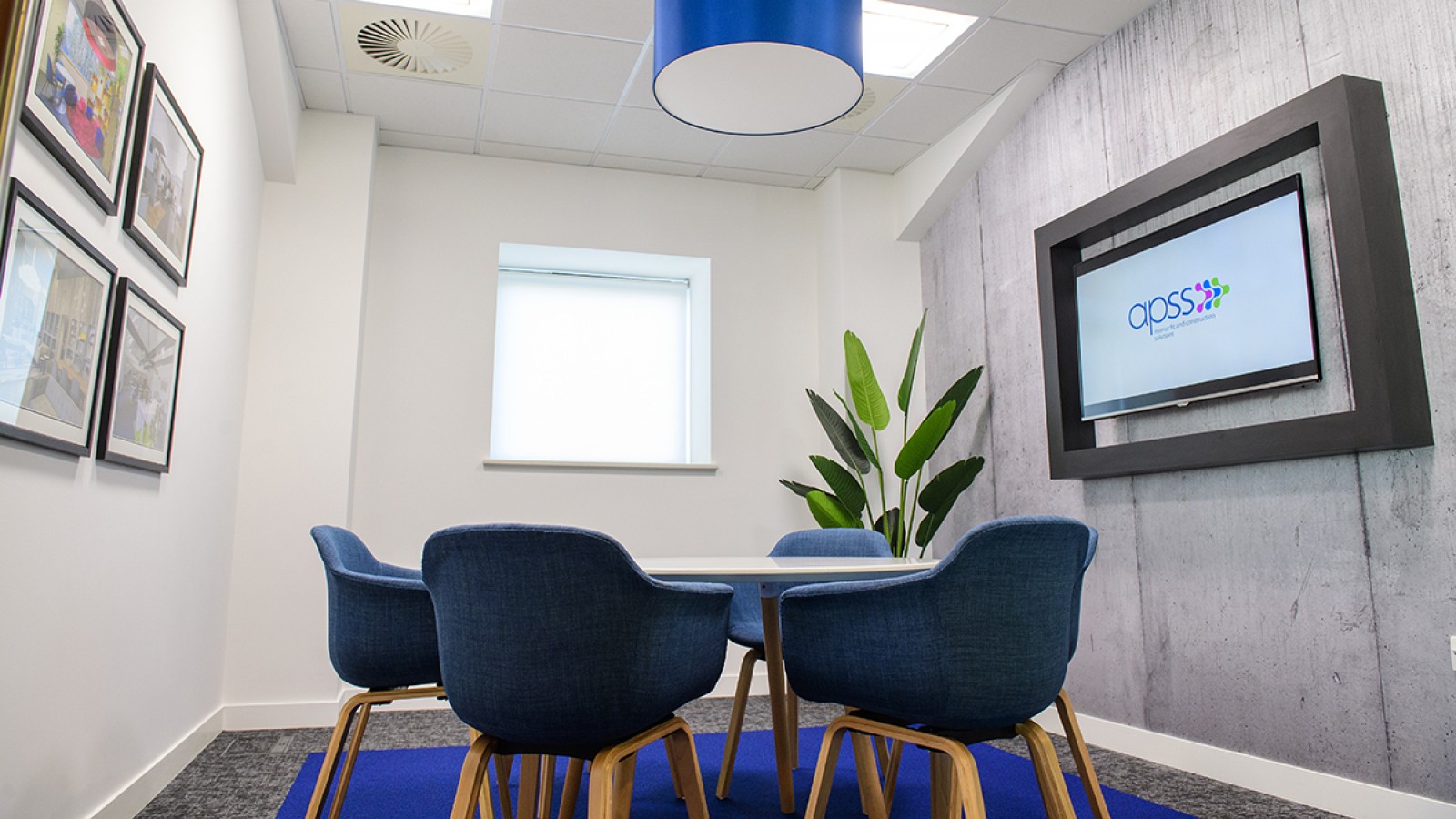The interior of a newly refurbished office, with a table, chairs, feature wall with text, and screen showing APSS logo