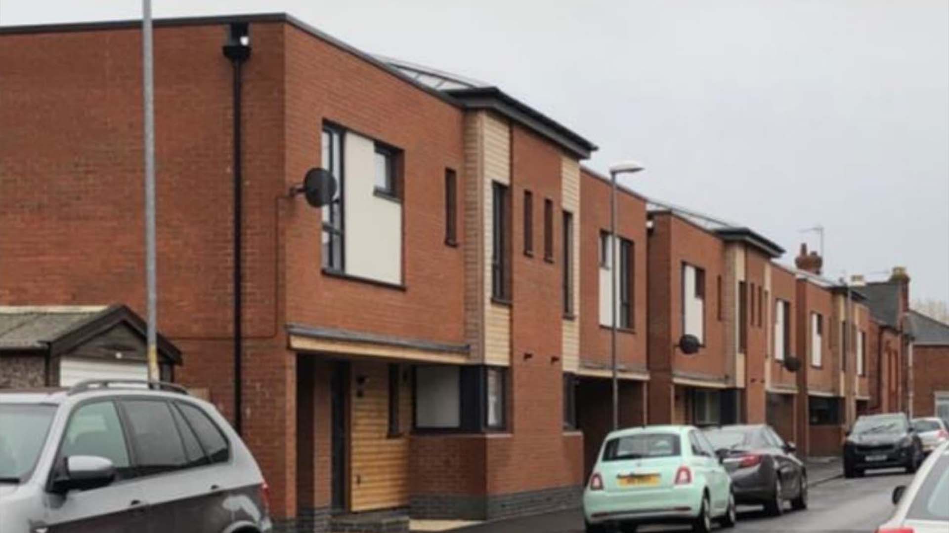 A wide shot of a street with several cars parked on the road. The sky is gret