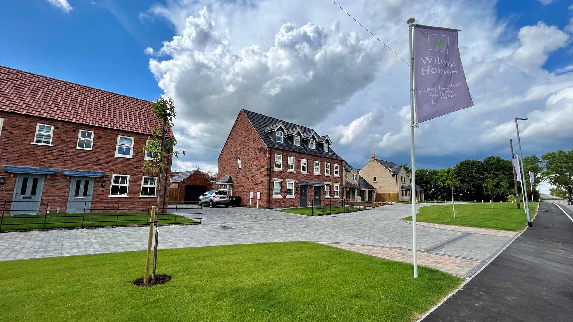 A wide shot of a newly built house. On the front lawn is a flag with the words 'Wilcox Homes'